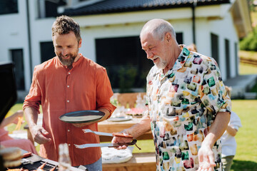 Senior father with adult son grilling outside on backyard in summer family during garden party
