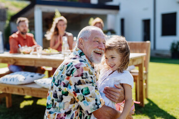 Happy little girl giving birthday present to her senior grandfather at generation family birthday party in summer garden - Powered by Adobe