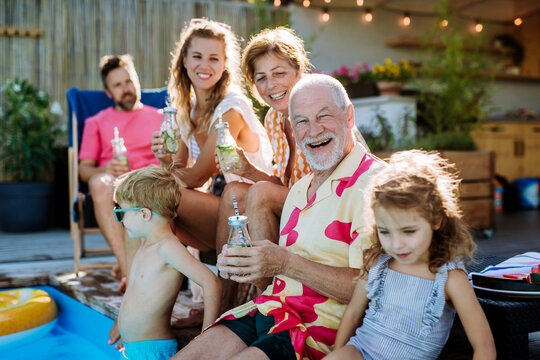 Multi generation family enjoying summer time, sitting at backyard pool.