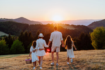 Happy young parents with daughters walking for picnic in nature in summer day,
