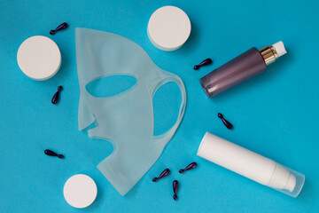 Cosmetics for face and body care with cosmetic silicone mask on blue background, mockup. Health care concept. Top View.