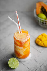 Tropical summer smoothie on a light background. Drink Lassi made of yogurt, papaya, mango, other tropical fruits, spices and ice. Close-up.