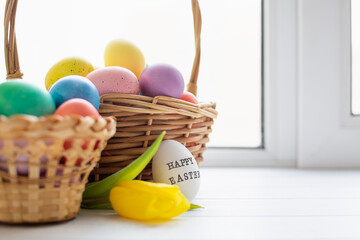 Wicker baskets with bright colorful eggs and with text Happy Easter and flower
