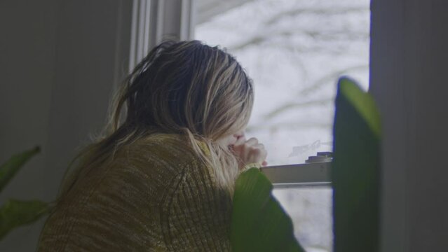 A disheveled woman grips a window pane as she battles depression