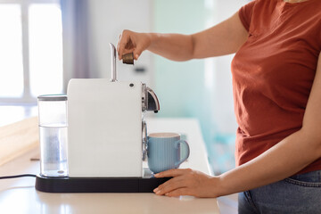 Side view of woman inserting coffee capsule in espresso machine in kitchen