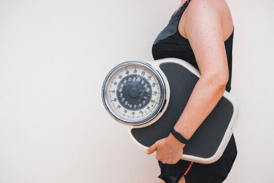 A woman in a sports outfit holds a professional scale under her arm, Concept, Spring weight loss, Healthy lifestyle, Positive attitude and changing bad habits