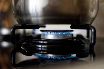 Metalowy garnek na kuchni gazowej z palącym się palnikiem blekitnego paliwa - obrazy, fototapety, plakaty