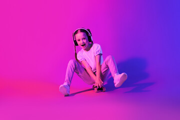 Emotional cute school-aged girl posing with skateboard on studio background