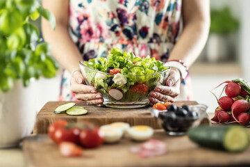 A view of a young woman's hands holding a glass bowl full of a healthy mixed salad