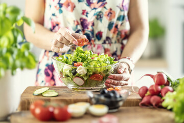 A woman prepares a healthy salad and puts a sliced tomato in a bowl