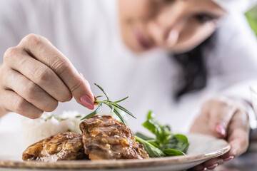 Close-up view of chef's fingers with rosemary sprig decorating food in restaurant kitchen