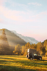 Camperized 4x4 off-road car in a valley with amazing landscape views of forest, mountains and sun rays during sunrise. Van road trip holiday and outdoor summer adventure. Nomad lifestyle concept