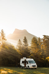 Camper van in a valley with amazing landscape views of forest, mountains and sun rays during...
