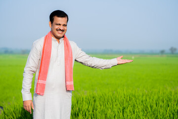 Happy smiling indian village farmer showing crop by looking at camera at paddy farmland - concept...