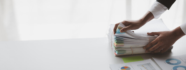 Businessman looking through stacks of papers on desk, corporate financial papers, monthly financial summary papers. Concept of document management in the organization.