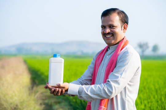 Happy Indian village farmer holding fertilizer bottle by looking at camera at farmland - concept of product promotion, recommendation and agricultural