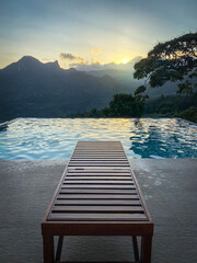 Wooden lounger beside an infinity pool at dusk. Jungle and cloud forest valley in the background in the evening.