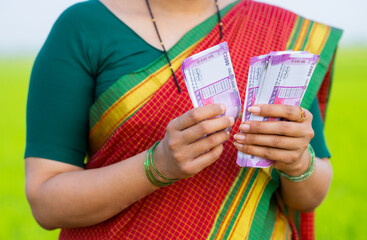 Close up shot of Indian woman hands counting money or currency notes at green farmland - concept of profit, banking and agriculture investment