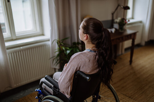 Unhappy teenage girl sitting on a wheelchair and looking out of the window.