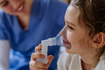 Little girl with inhaler in hospital room, nurse chcecking her.