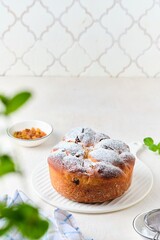 Twisted yeast cake with raisins sprinkled with powdered sugar on a white ceramic board against a light concrete background. Easter concept.