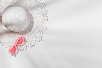 White sun hat and pink colored sunglasses on white background at sunlight with palm leaf shadows. Summer vacation, summertime relaxation concept, minimal trend flat lay, copy space. Top view