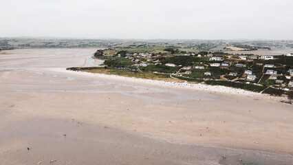Fototapeta na wymiar A small Irish village on a green hill near a large sandy beach, top view. Aerial view of city