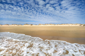 White foam of wave entering beach with dunes and sky with cirrocumulus clouds