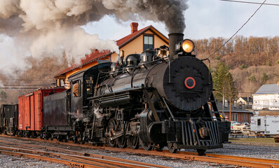 Fototapeta premium View of a Restored, Antique Steam Freight Train Approaching in Early Morning, on old Narrow Gauge Tracks on a Winter Day, Blowing Smoke