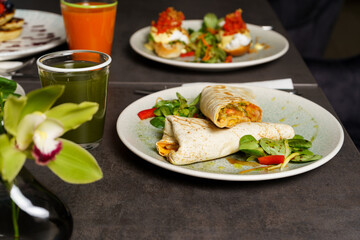 Wrapped Burrito with Beans and Vegetables on a Plate, carrot juice on the table