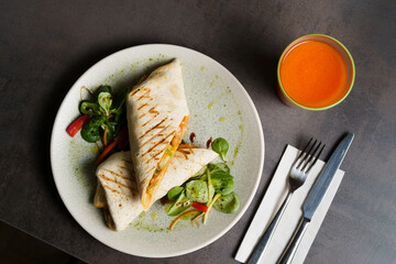 Top Down View of Burrito with Beans and Vegetables on a Plate, carrot juice on the table