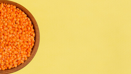 Red raw lentils in a wooden bowl on a yellow background. Top View. Place for text. Healthy food.