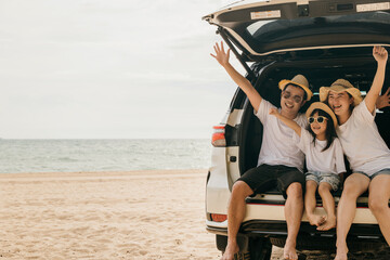 Happy Family Day. Dad, mom and daughter enjoying road trip sit on back car and raise hand up,...