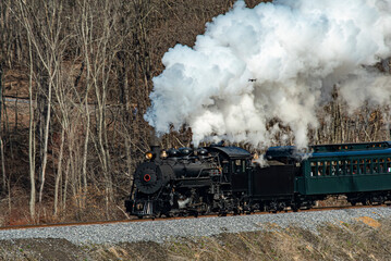 Fototapeta na wymiar View of a Narrow Gauge Restored Steam Passenger Train Blowing Smoke and Traveling Thru Farmlands on a Winter Day
