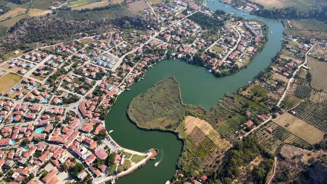 Aerial drone video capturing the charming town of Dalyan in Ortaca, Muğla, Turkey, featuring boats cruising along the scenic canal that runs through the town.