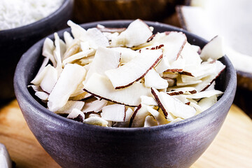 coconut chips, shavings and pieces of coconut inside a clay bowl, with many ripe coconuts in the...