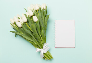 White tulip bouquet with notebook on color background, top view