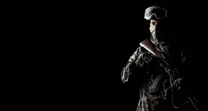 A masked soldier holds a rifle in his hands on a black background, alone