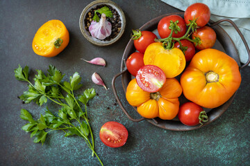Various colorful tomatoes and parsley leaves on a dark stone background. Organic food. View from above.