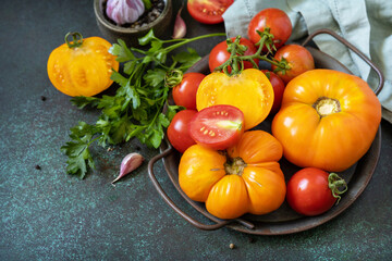 Organic food. Various colorful tomatoes and parsley leaves on a dark stone background. Copy space.