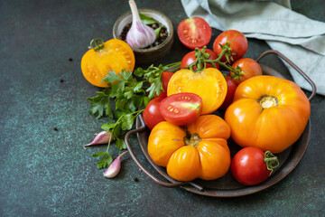 Various colorful tomatoes and parsley leaves on a dark stone background. Organic food. Copy space.