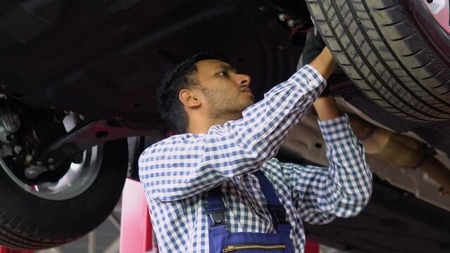 Professional Indian Repairman is Wearing Gloves and Using a Ratchet Underneath the Car. Modern Clean Workshop