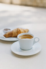 Cup of black coffee and a croissant on a table in a street cafe.