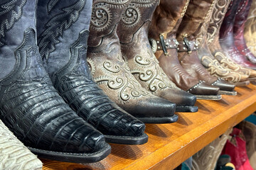 Collection of cowboy boots stand on a wooden shelf in store in texas, western shoes at ranch.