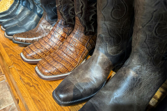 Collection of leather handmade cowboy boots stand on a wooden shelf in store in texas, western shoes at ranch.