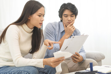 Stressed financial owe asian young couple love hand in holding bills, sitting on sofa together, stressed and confused by calculate expense, mortgage or loan. Debt, bankrupt or bankruptcy people.