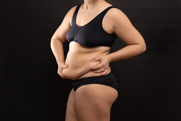 Overweight woman in black underwear massaging belly fat folds by hands, side view. Flaunt figure...