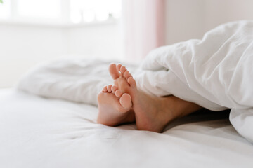 Obraz na płótnie Canvas Feet of little girl on bed under white blanket, sleep at morning.