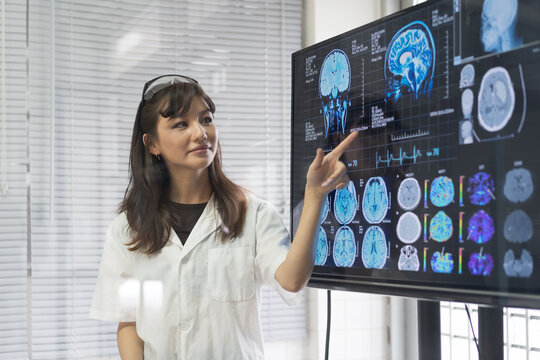 Female medical scientists presenting in brain research laboratory by monitor showing MRI, CT scans brain images. Female doctor wear uniform showing magnetic resonance image (MRI) of brain project