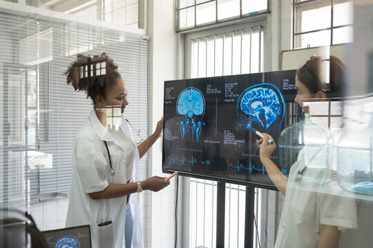 Team of female medical scientists presenting in brain research laboratory by monitor showing MRI, CT scans brain images. Female doctor showing magnetic resonance image (MRI) of brain project